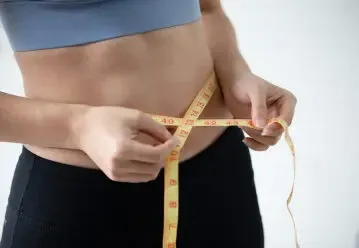 Woman measuring waist with tape measure during weight loss program at Dolce MD clinic in Laguna Beach, CA